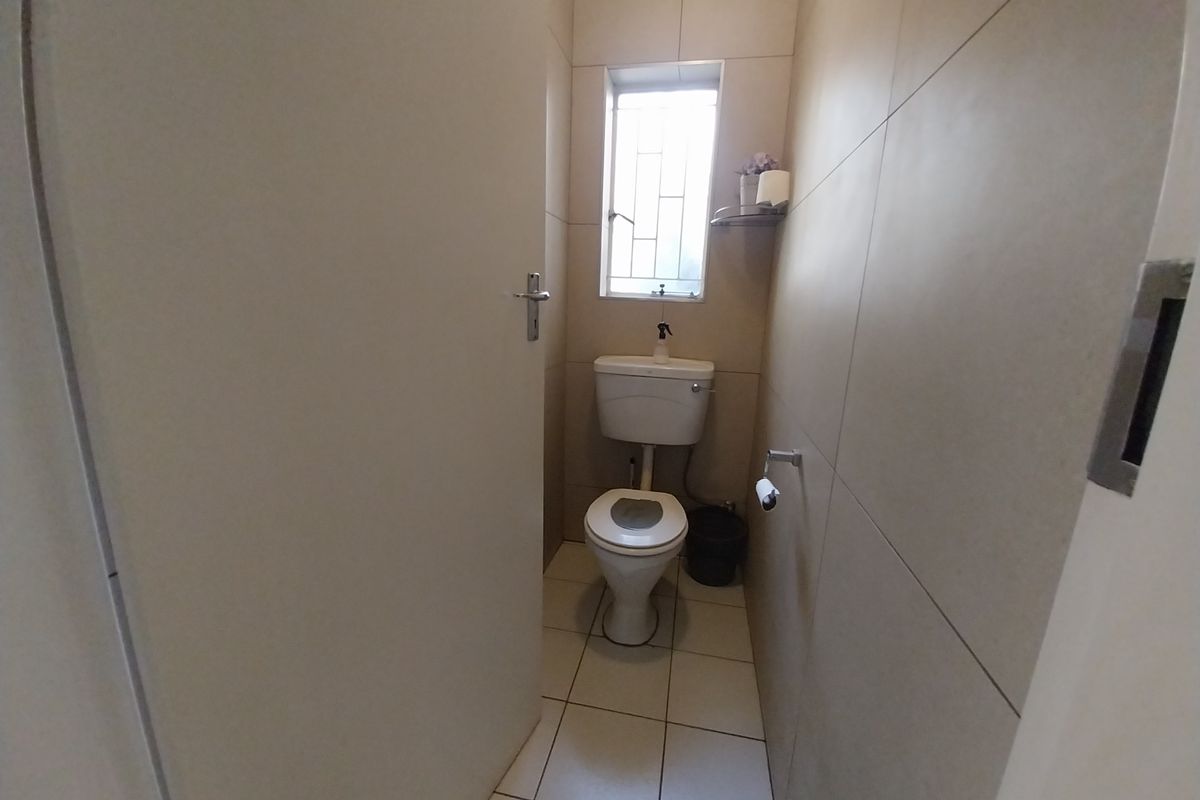 A compact guest toilet featuring neutral floor-to-ceiling wall tiles, tiled flooring, and a window with security bars.