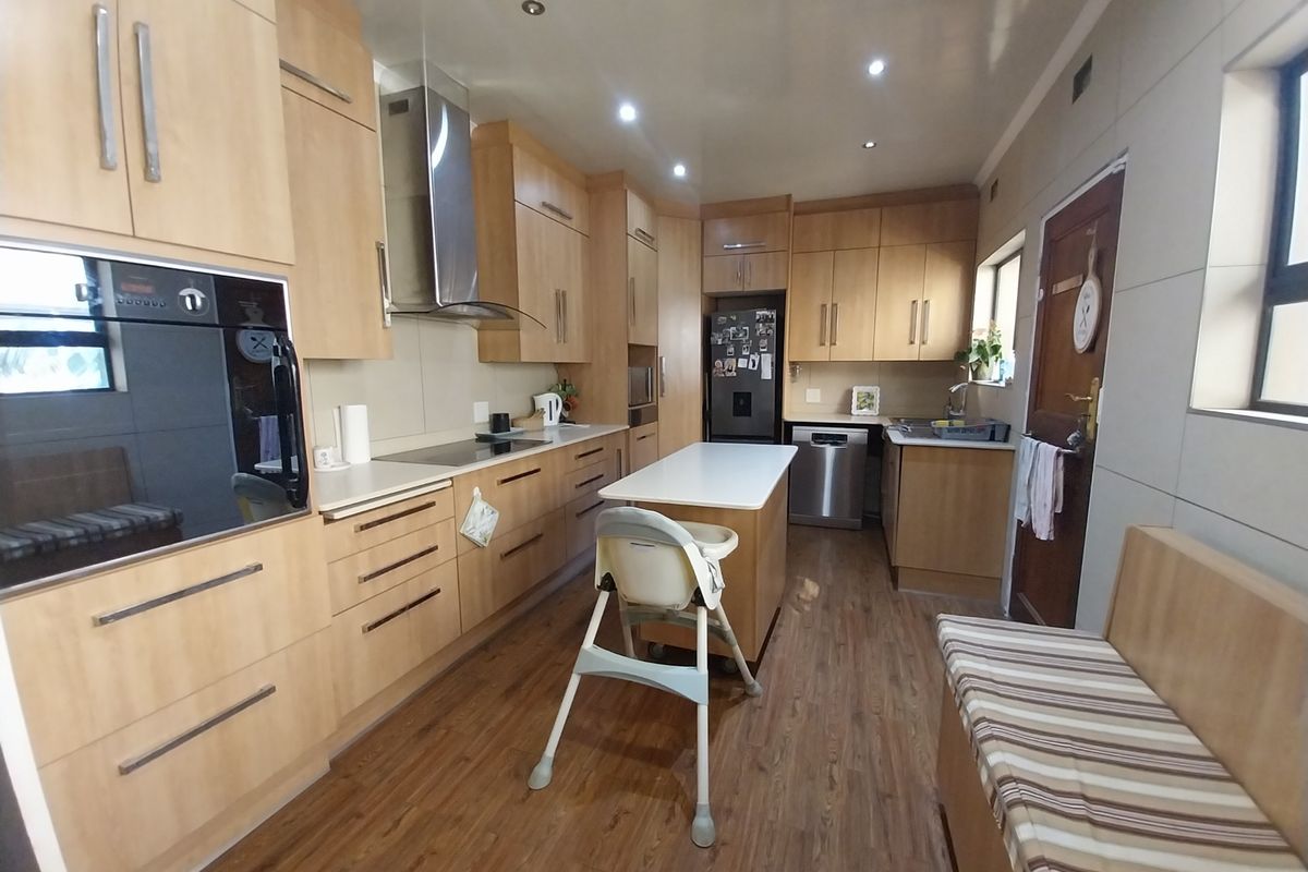 A functional kitchen featuring light wood cabinetry, a central island, built-in oven, extractor fan, and integrated dishwasher, finished with wood-look flooring.