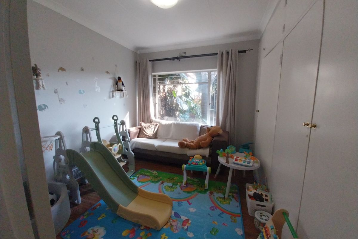 A bedroom featuring built-in cupboards, wooden flooring, and a large window providing natural light, currently utilized as a children's play area.