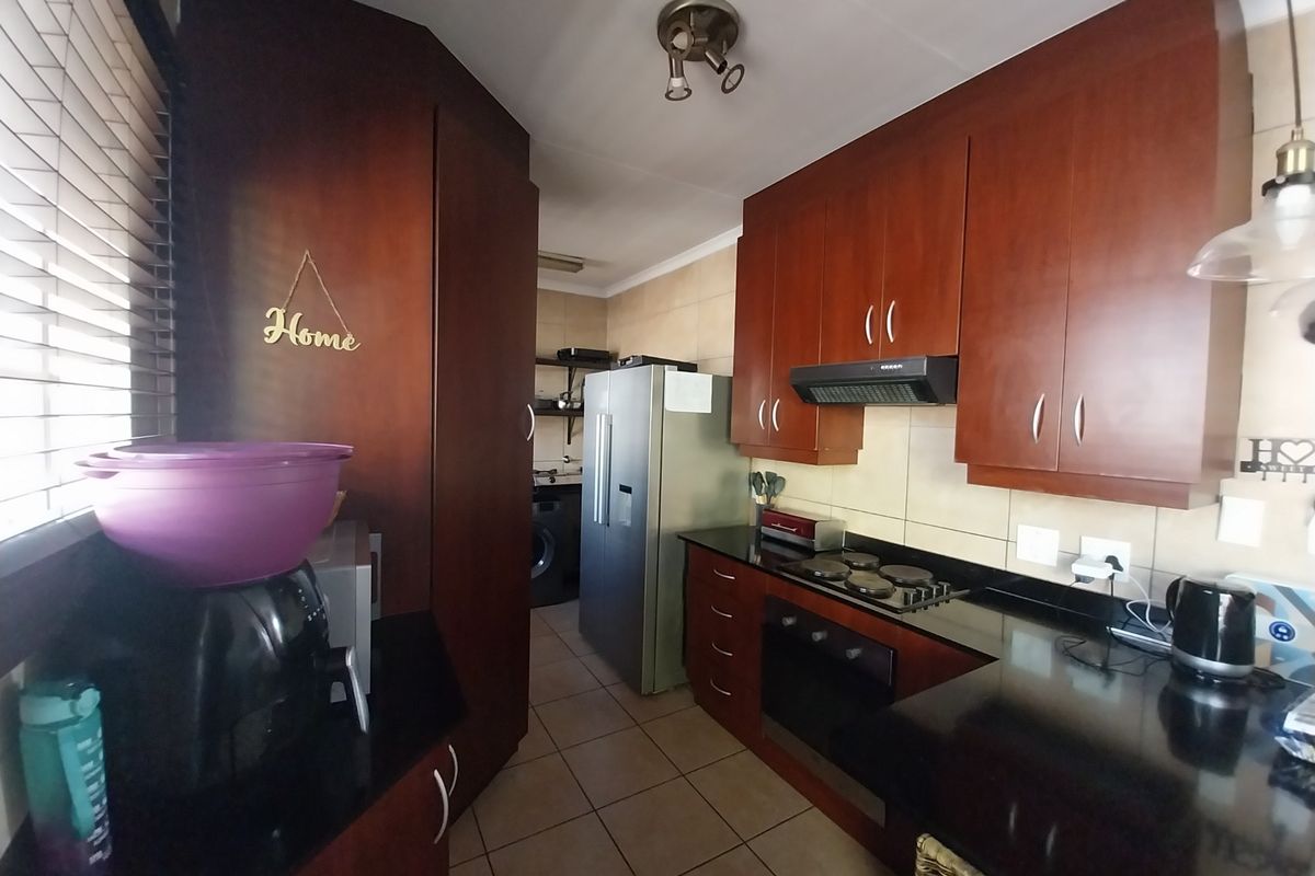 A functional kitchen featuring dark wood cabinetry, black granite countertops, a built-in oven, hob, and extractor fan, with tiled flooring throughout.