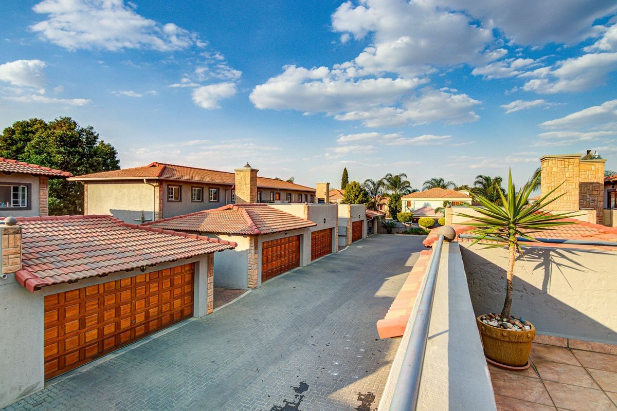 Elevated view of a townhouse complex driveway featuring multiple wooden garage doors, tiled roofs, and stone-clad chimney stacks.