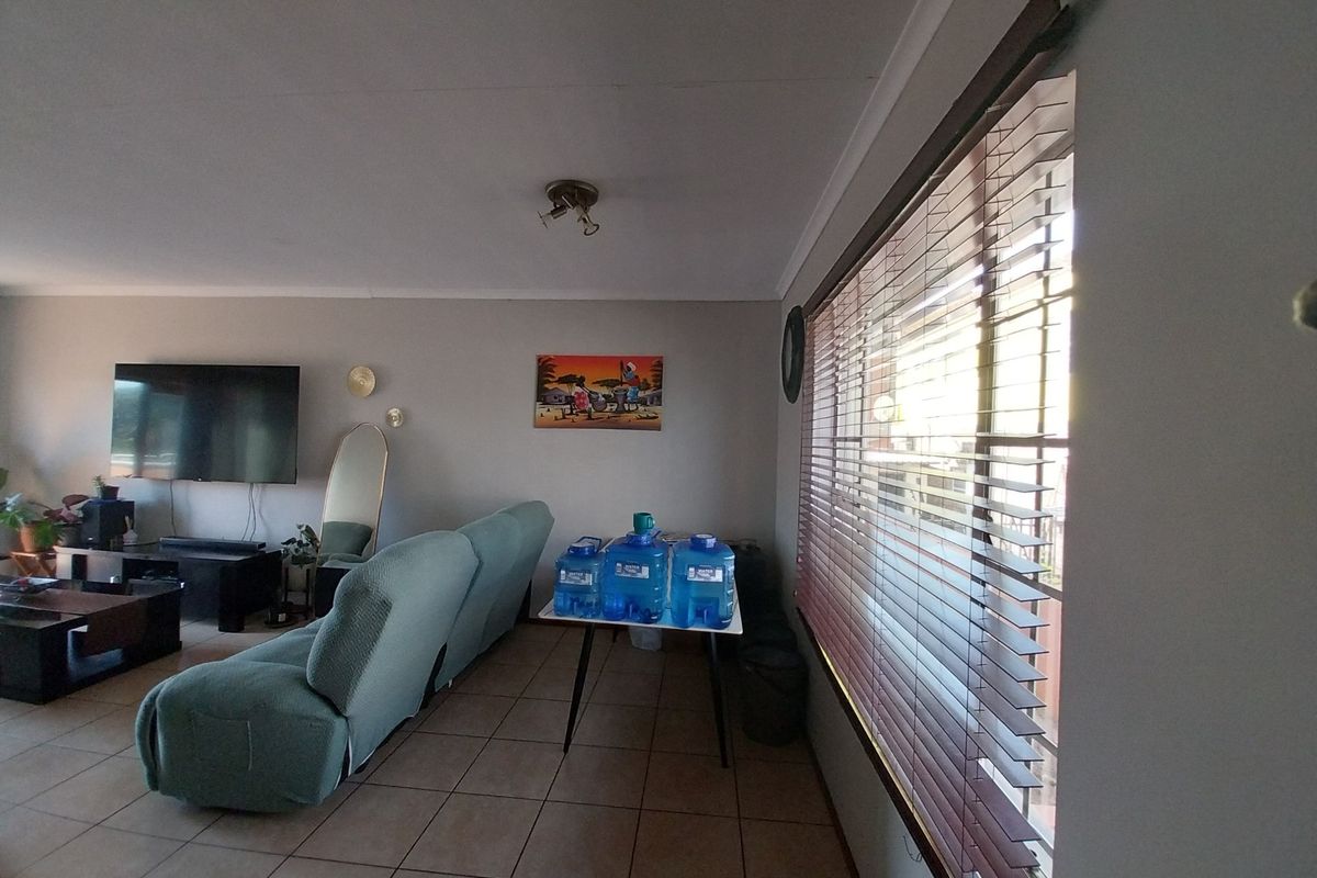 A spacious living room featuring tiled flooring, large windows with fitted blinds, and neutral wall finishes.