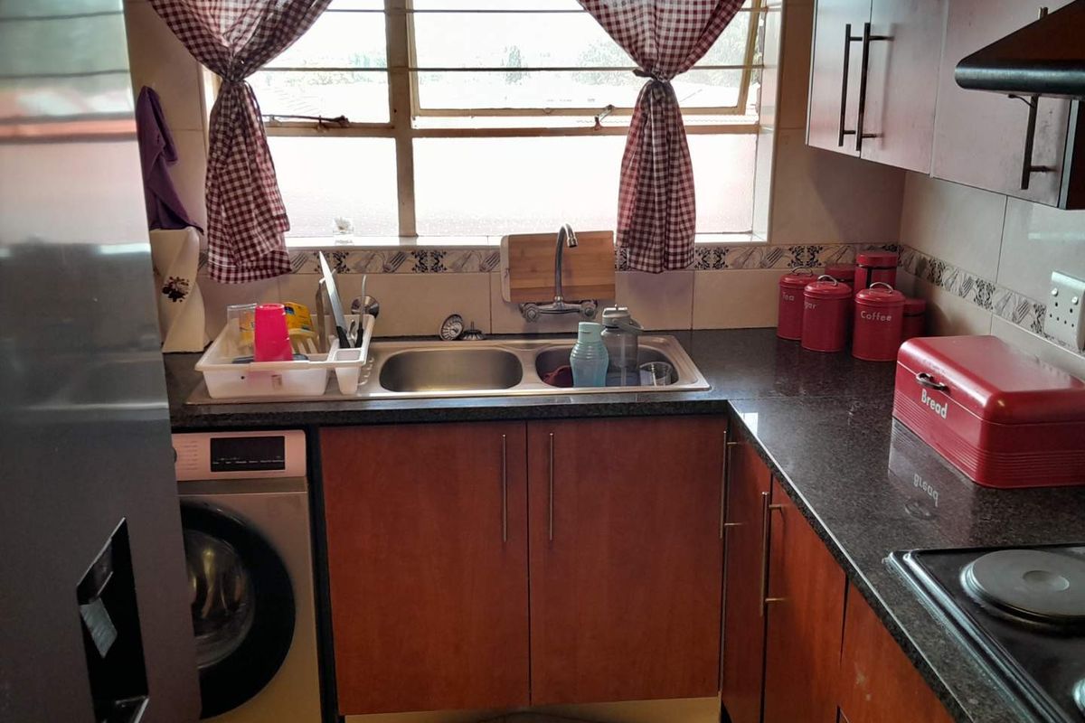 Compact kitchen featuring dark granite countertops, wooden cabinetry, a double stainless steel sink, and integrated space for a washing machine.
