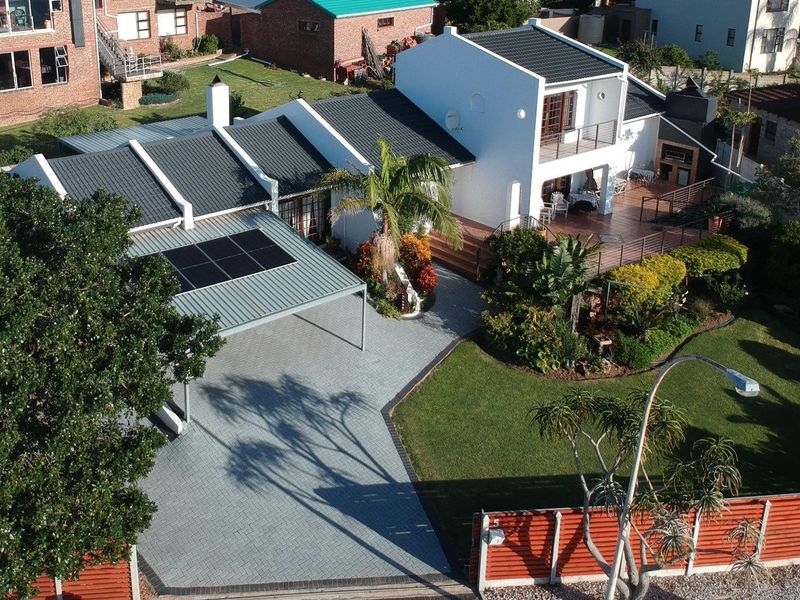 Aerial view of a well-maintained residential property featuring a paved driveway, carport with solar panels, landscaped garden, and a spacious rear patio with braai.