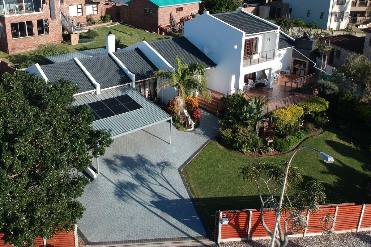 Aerial view of a well-maintained residential property featuring a paved driveway, carport with solar panels, landscaped garden, and a spacious rear patio with braai.