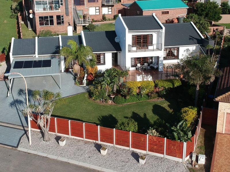 Aerial view of a well-maintained residential property featuring a tiled roof, solar panels, paved driveway, carport, and a landscaped garden with timber fencing.