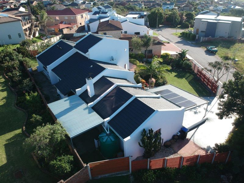 Aerial view of a residential property featuring a tiled roof, solar panels, a water storage tank, and a well-maintained garden with perimeter fencing.