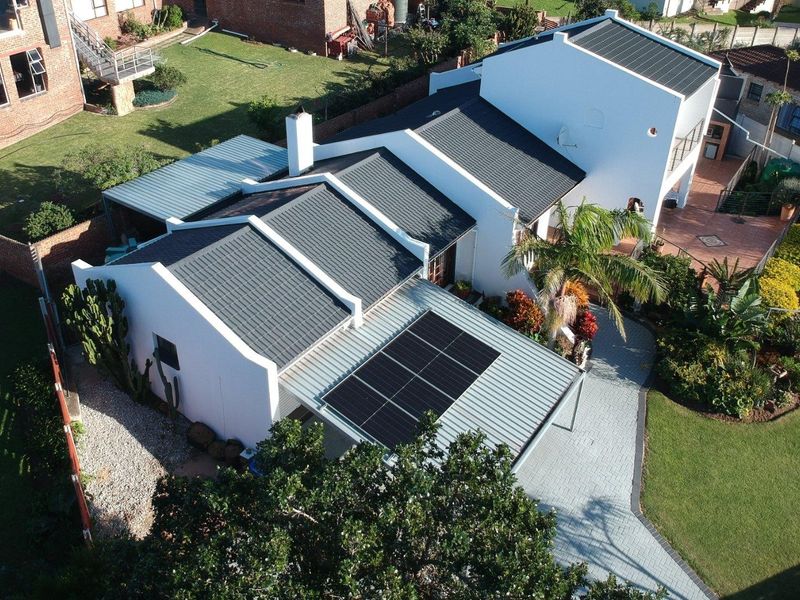 Aerial view of a residential property featuring a well-maintained roof with integrated solar panels, a paved driveway, and landscaped garden areas.
