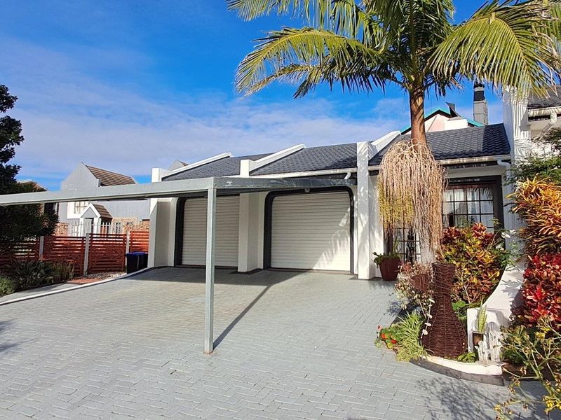 Front exterior view featuring a paved driveway, double garage with roller shutter doors, and a covered carport area.