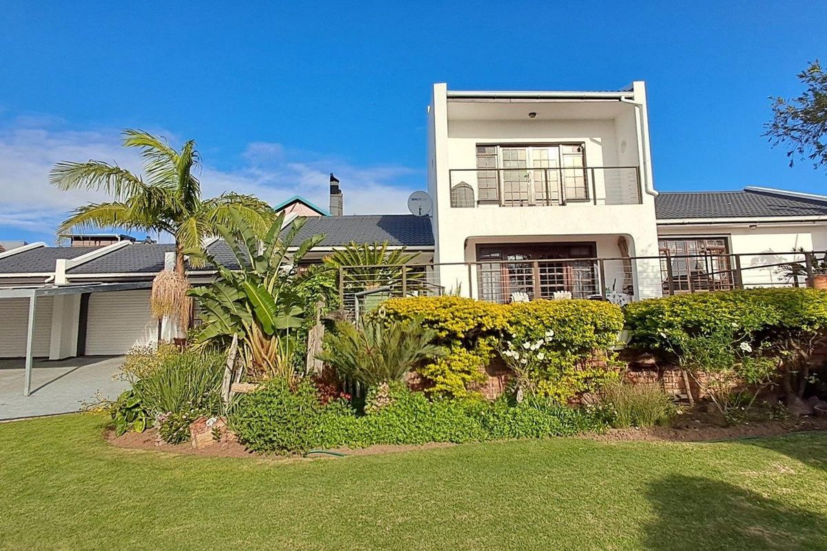 Rear view of a multi-level house featuring a landscaped garden, balcony with metal railings, and a double garage.