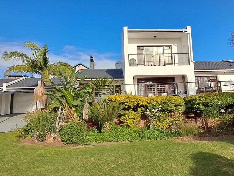 Rear view of a multi-level house featuring a landscaped garden, balcony with metal railings, and a double garage.