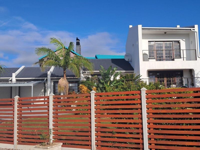 Front view of a multi-level residential property featuring a timber slat fence, tiled roof, and an upper-level balcony.
