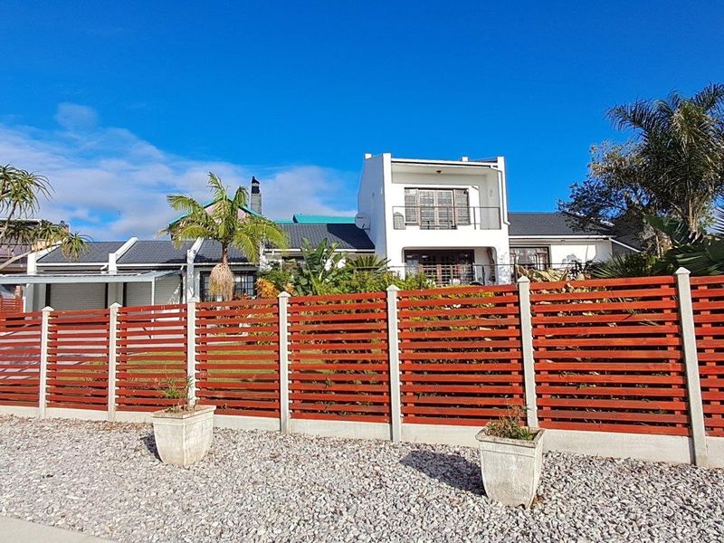 Front view of a multi-level residential property featuring a modern slatted timber fence, gravel driveway, and a prominent balcony.