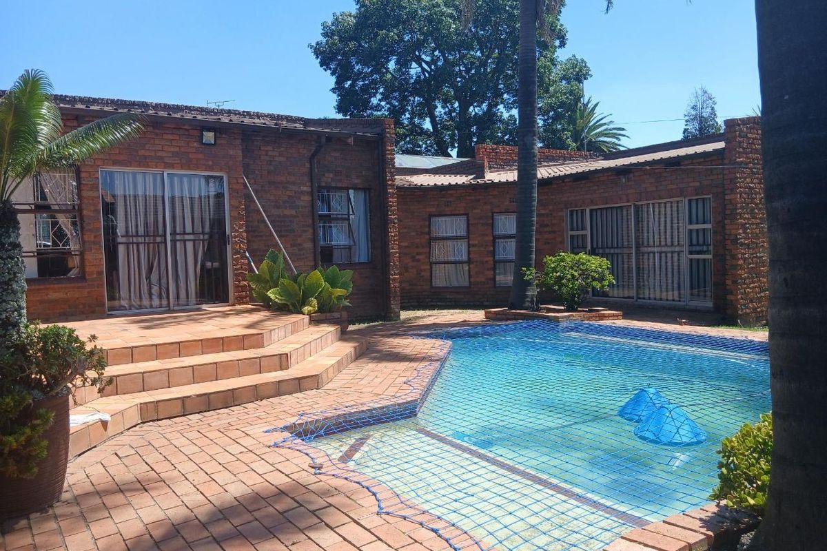 Rear exterior view featuring a brick-built house with a swimming pool, paved patio area, and sliding glass doors leading to the interior.