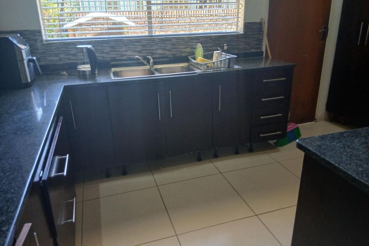 A functional kitchen featuring dark cabinetry, granite-style countertops, a double stainless steel sink, and tiled flooring with a window providing natural light.