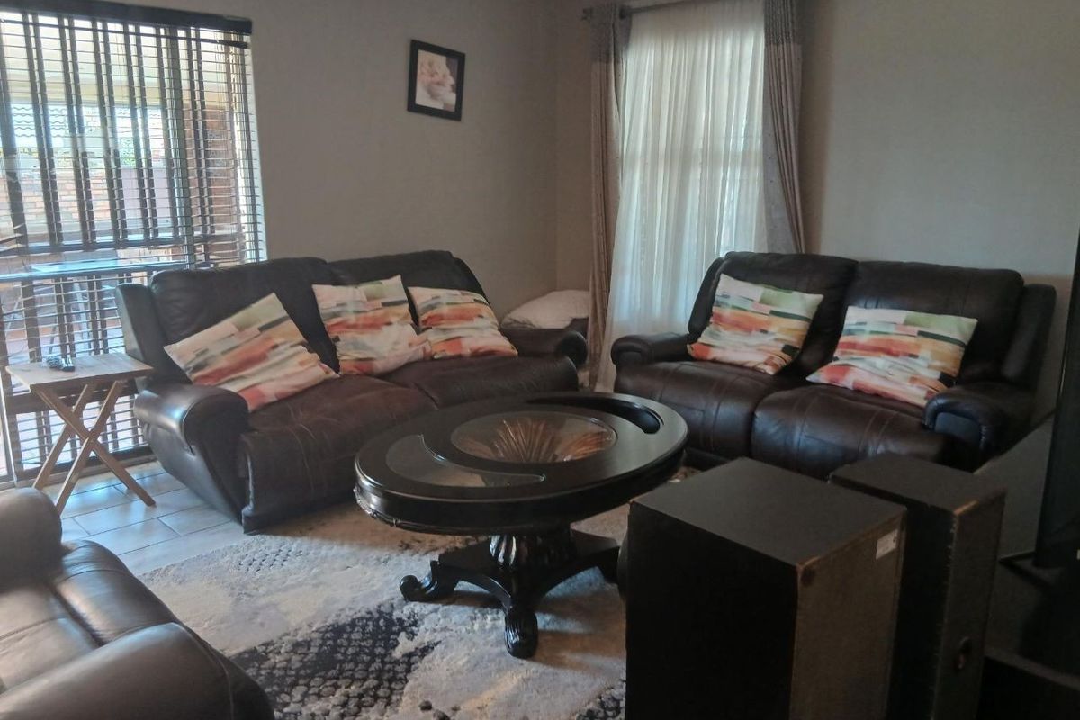 A comfortable living room featuring tiled flooring, large windows with blinds and curtains, and neutral wall finishes.