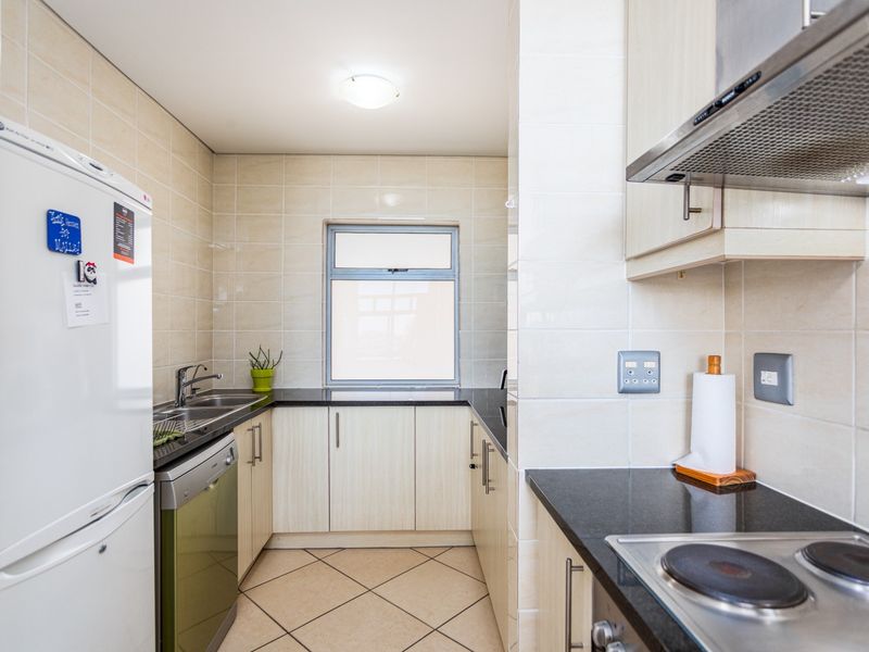 A functional kitchen featuring light-toned cabinetry, dark granite countertops, tiled walls, and built-in cooking appliances including a hob and extractor fan.