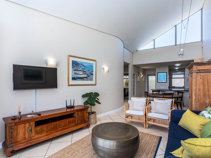 Spacious open-plan living and dining area featuring a unique curved wall, high vaulted ceilings with clerestory windows, and tiled flooring throughout.