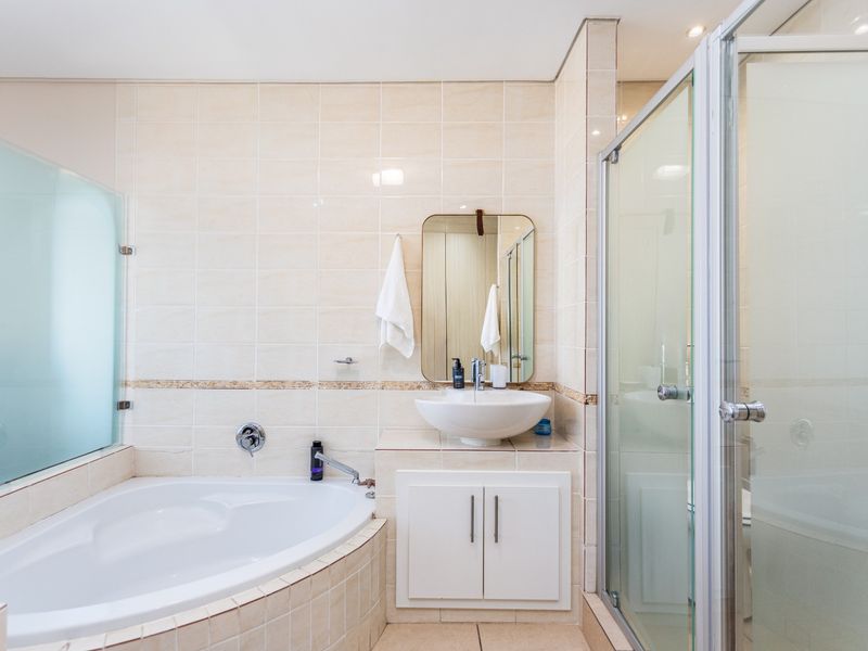 A functional bathroom featuring a corner bathtub, a separate glass-enclosed shower, and a vanity basin with built-in cabinetry.