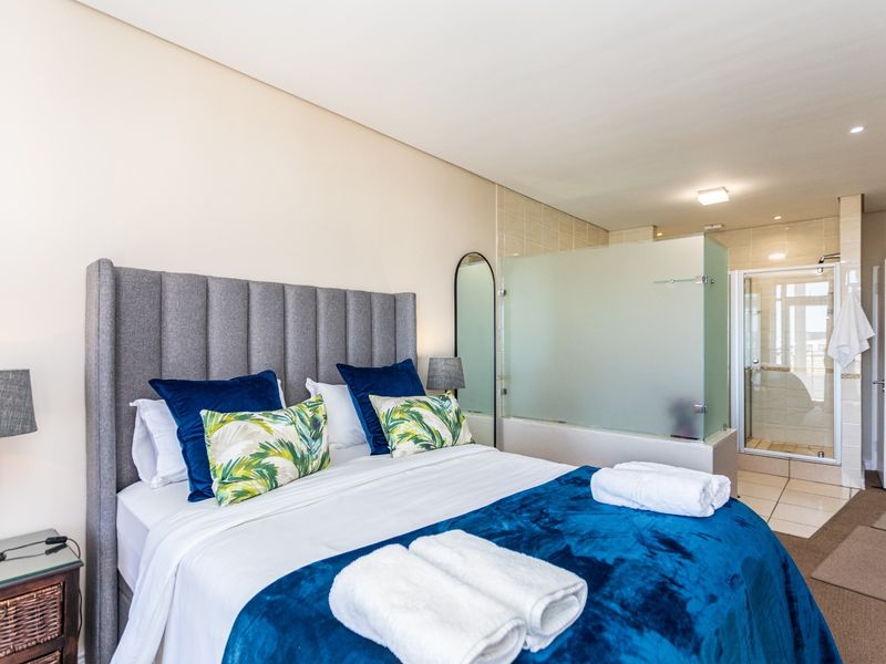 A well-appointed bedroom featuring an open-plan en-suite bathroom with a glass-enclosed shower and tiled flooring.