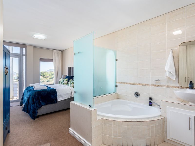 Open-plan bedroom featuring an integrated en-suite bathroom with a corner soaking tub, vanity basin, and glass privacy screen.