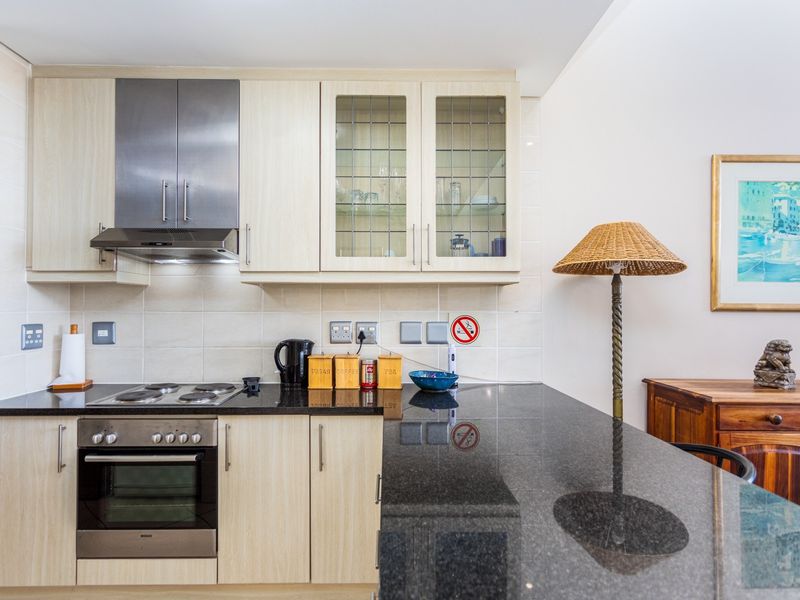 A well-maintained kitchen featuring light wood cabinetry, black granite countertops, a built-in oven, electric hob, and a stainless steel extractor fan.