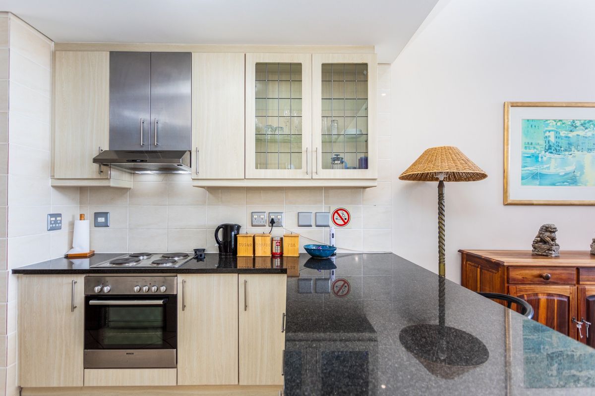 A well-maintained kitchen featuring light wood cabinetry, black granite countertops, a built-in oven, electric hob, and a stainless steel extractor fan.