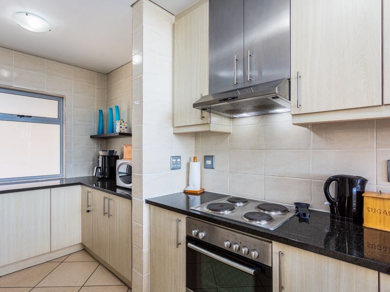 A functional kitchen featuring light wood cabinetry, dark granite countertops, a built-in oven, electric hob, and stainless steel extractor fan.
