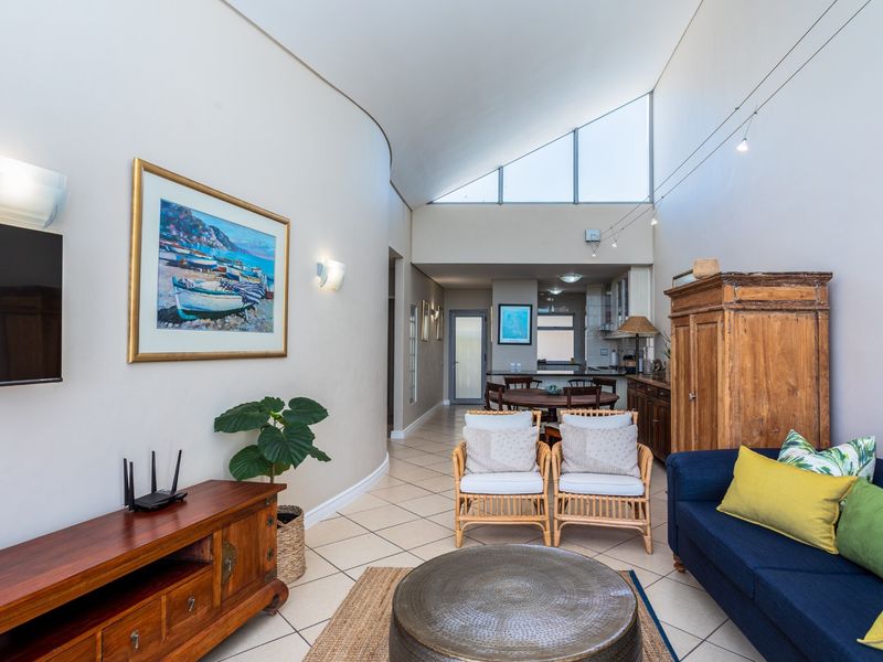 Open-plan living area featuring high vaulted ceilings, large triangular windows, tiled flooring, and a seamless transition to the kitchen and dining space.