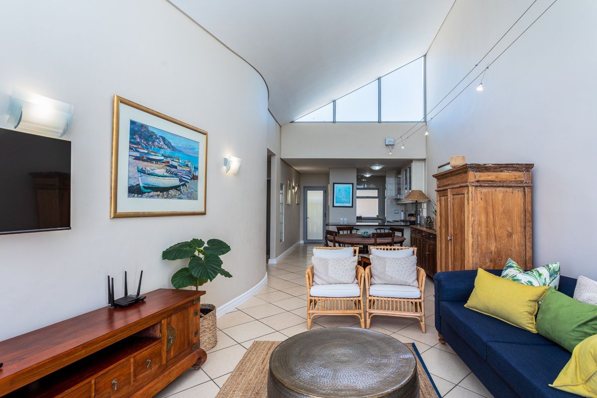 Open-plan living area featuring high vaulted ceilings, large triangular windows, tiled flooring, and a seamless transition to the kitchen and dining space.