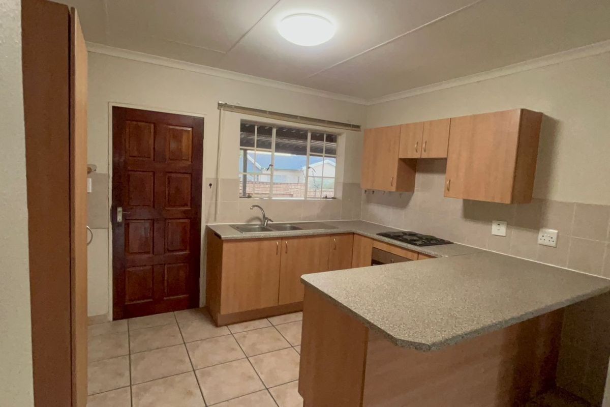 Functional kitchen featuring light wood cabinetry, laminate countertops, a built-in hob, and tiled flooring with direct access to the exterior.