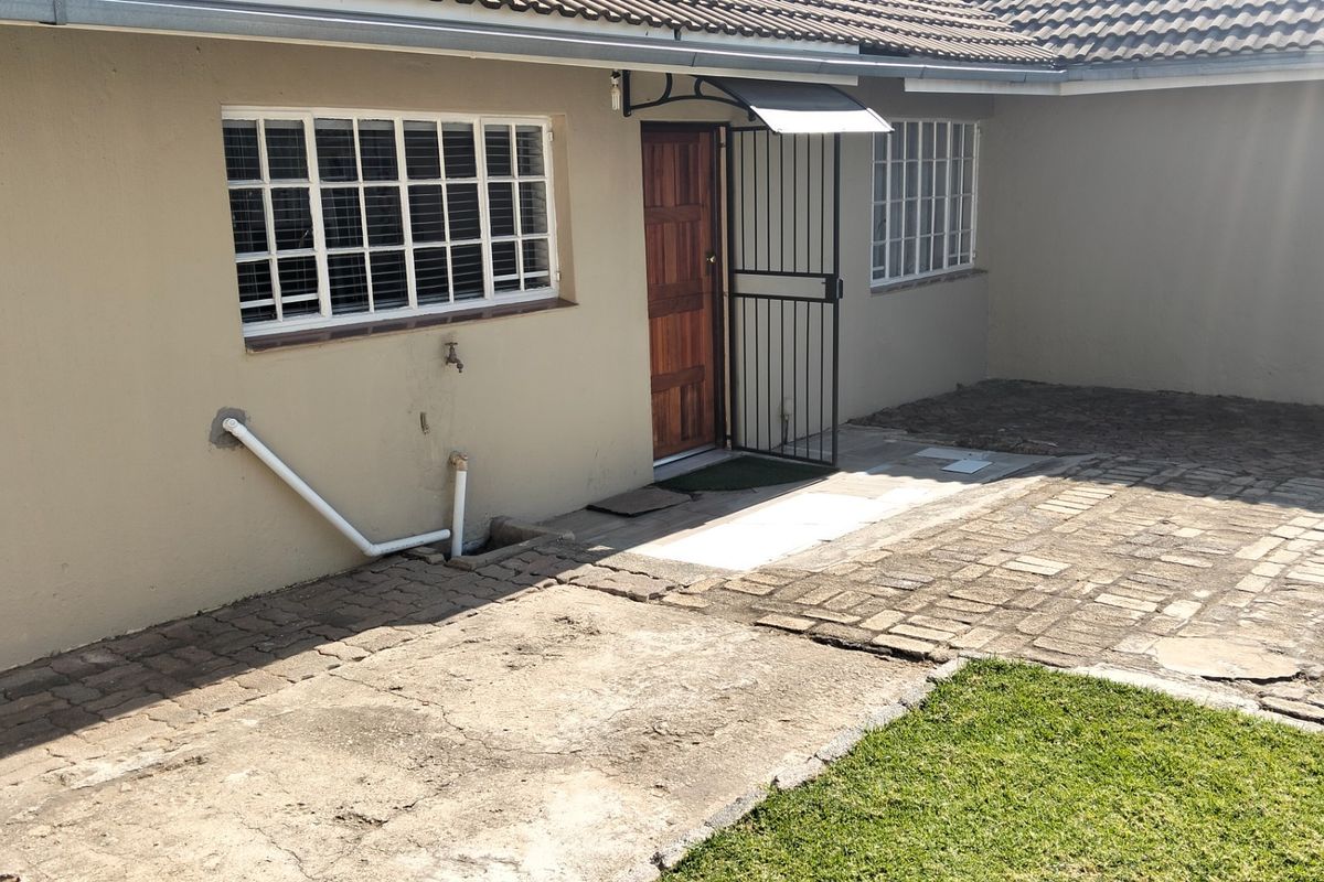 Rear exterior view of the property featuring a paved courtyard area, security gate, and access to the main dwelling.