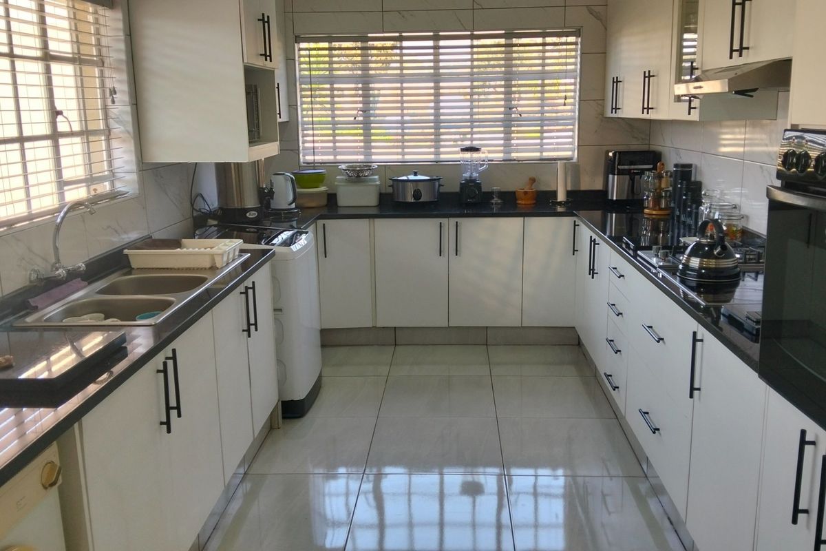 Modern U-shaped kitchen featuring white cabinetry, contrasting black granite countertops, tiled flooring, and integrated oven and extractor fan.