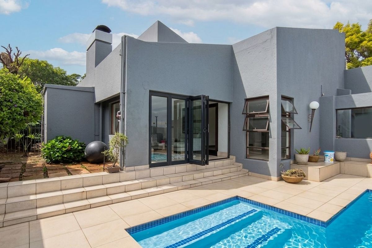 Rear exterior view featuring a modern swimming pool, tiled patio area, and bi-fold doors leading into the home.
