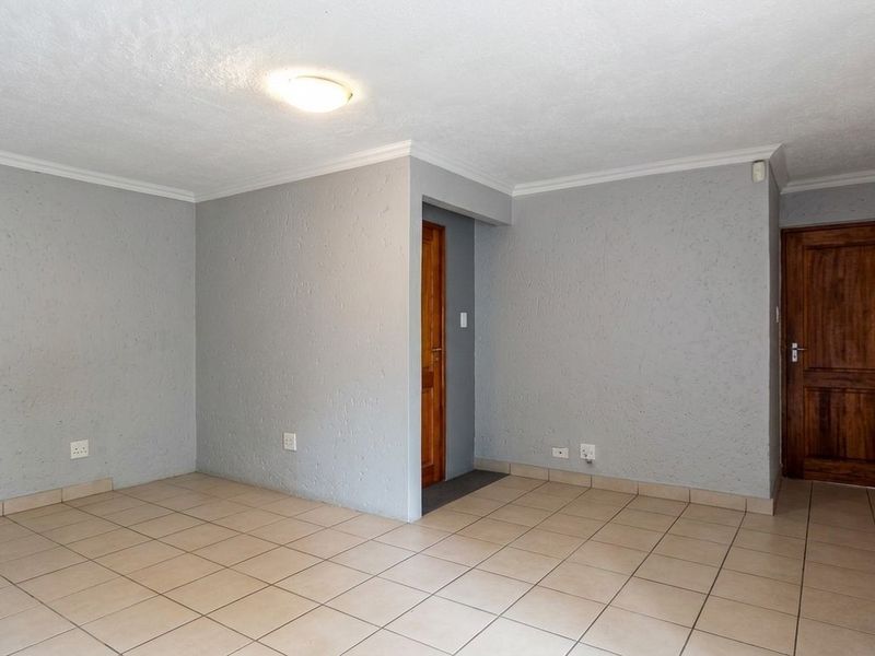 An empty, neutrally painted living area featuring tiled flooring, textured walls, and wooden doors, providing a blank canvas for interior design.