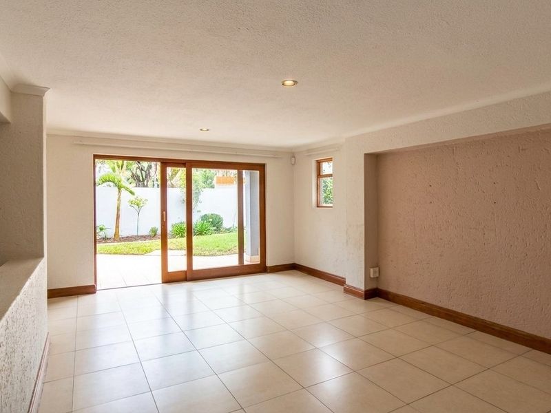 A bright, empty living room featuring tiled flooring, recessed lighting, and large sliding glass doors that open onto a private garden patio.