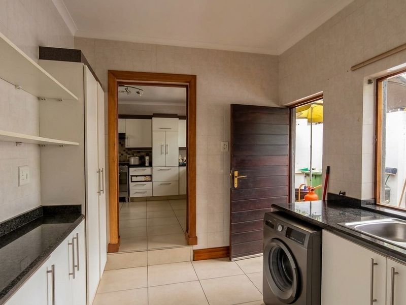 A functional scullery featuring tiled walls and floors, granite countertops, built-in cabinetry, and a double stainless steel sink with direct access to the kitchen.