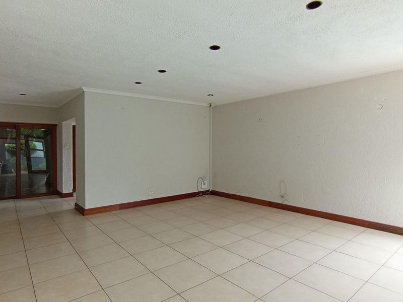 A spacious, empty living area featuring neutral tiled flooring, recessed downlights, and sliding glass doors leading to an outdoor space.