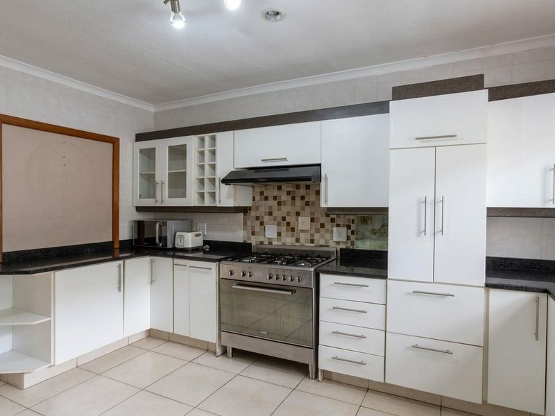 A functional kitchen featuring white cabinetry, dark granite countertops, a gas stove with extractor fan, and neutral tiled flooring.