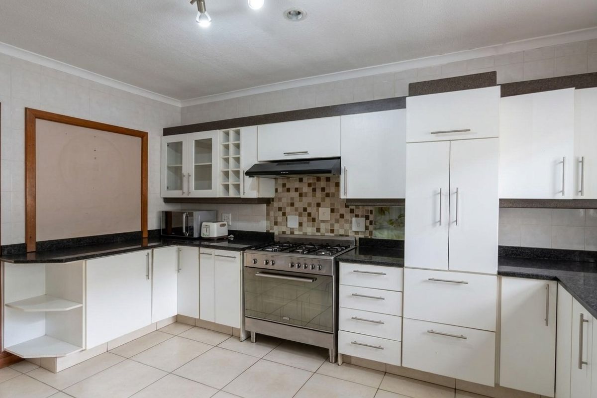 A functional kitchen featuring white cabinetry, dark granite countertops, a gas stove with extractor fan, and neutral tiled flooring.