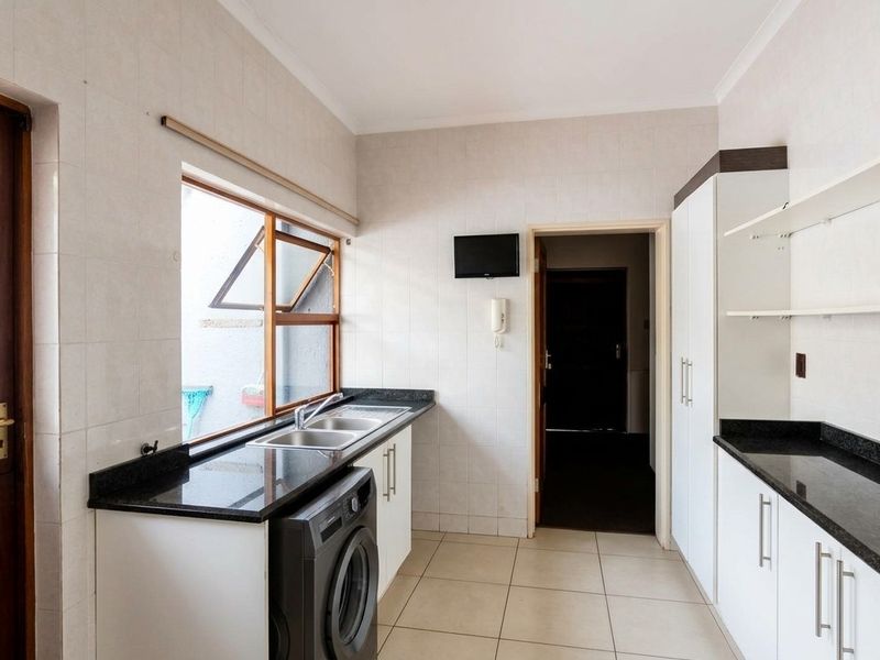 A functional laundry room featuring granite countertops, double basin sink, built-in cabinetry, and tiled finishes throughout.
