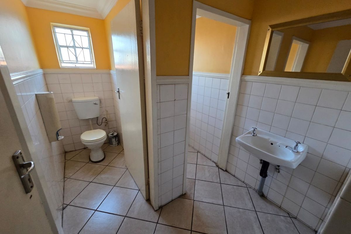 A functional office restroom featuring a wall-mounted basin, a standard toilet, and tiled flooring with half-tiled walls.