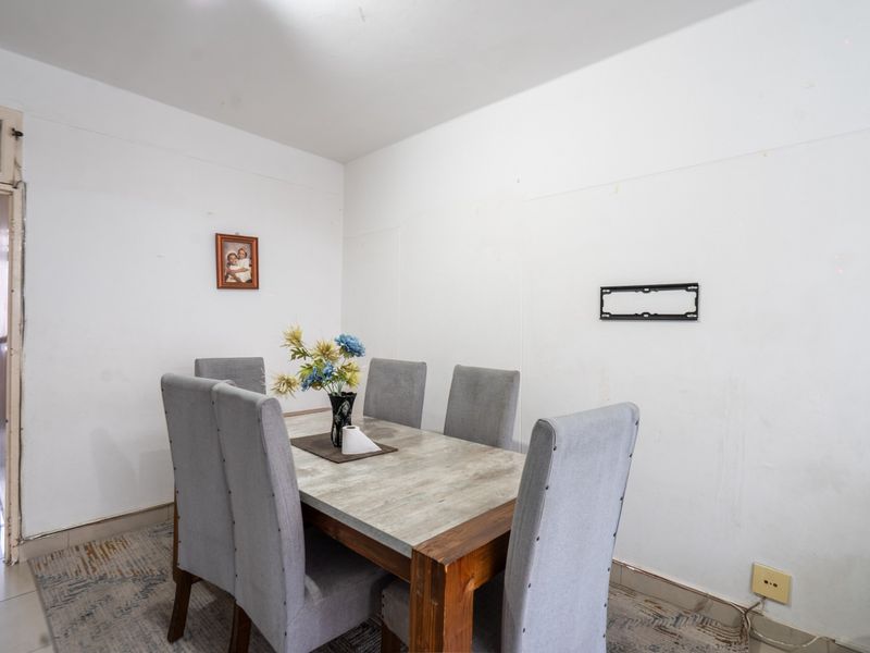 A dining area featuring plain white walls, a wall-mounted television bracket, and tiled flooring, providing a functional space for meals.