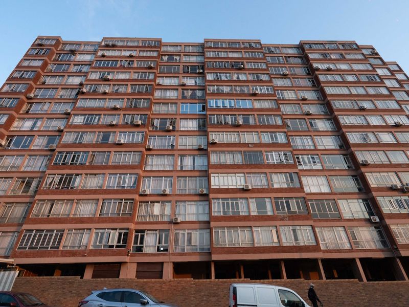A low-angle view of a large multi-story apartment building featuring a brick facade and numerous individual window units with external air conditioning installations.