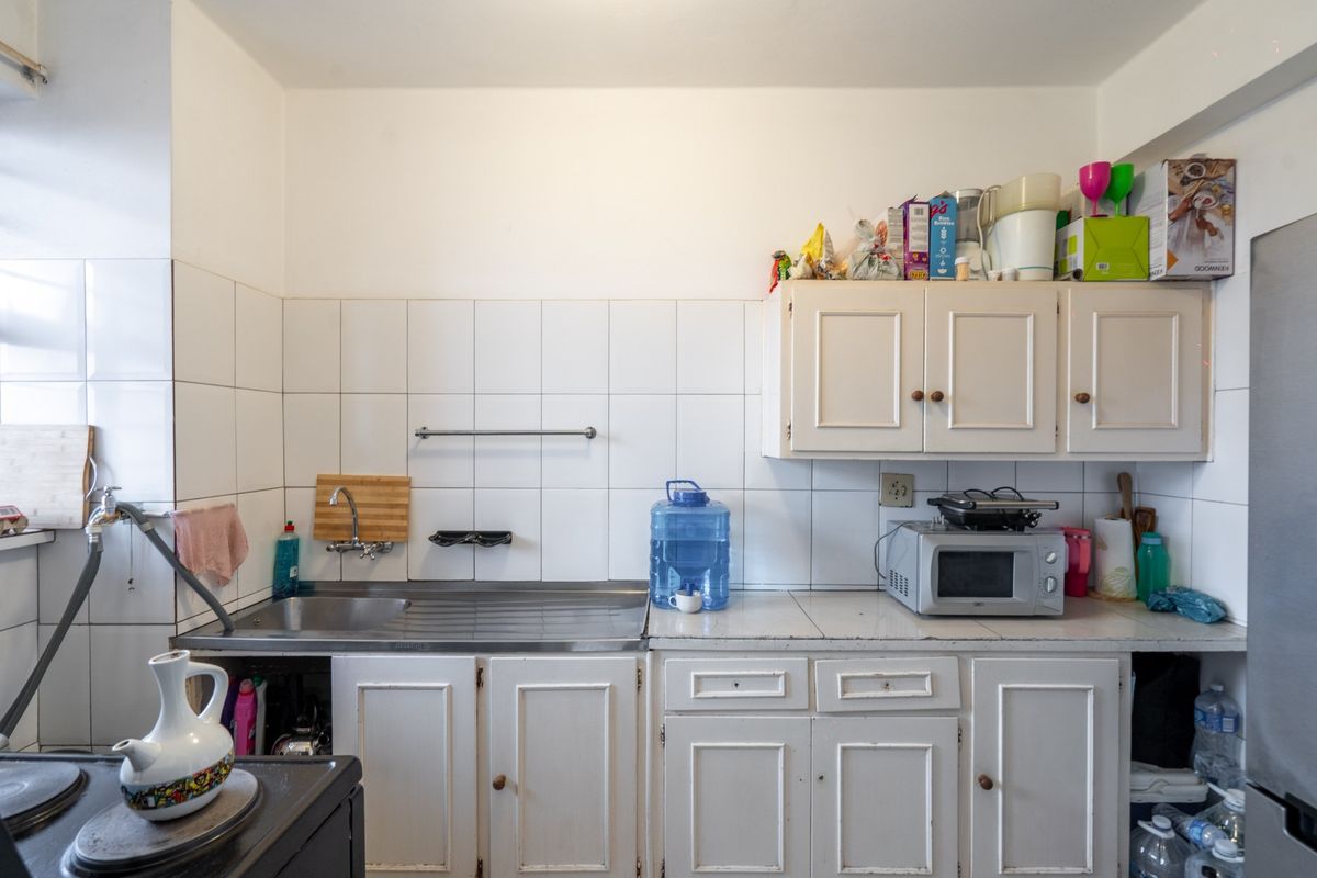 A functional kitchen area featuring white cabinetry, a stainless steel sink, and a tiled backsplash, offering a practical layout for daily use.