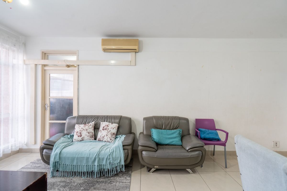 A living room featuring tiled flooring, a wall-mounted split-system air conditioner, and a glass panel door leading to an adjacent space.