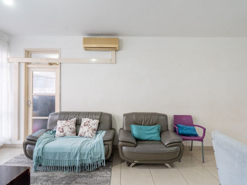 A living room featuring tiled flooring, a wall-mounted split-system air conditioner, and a glass panel door leading to an adjacent space.