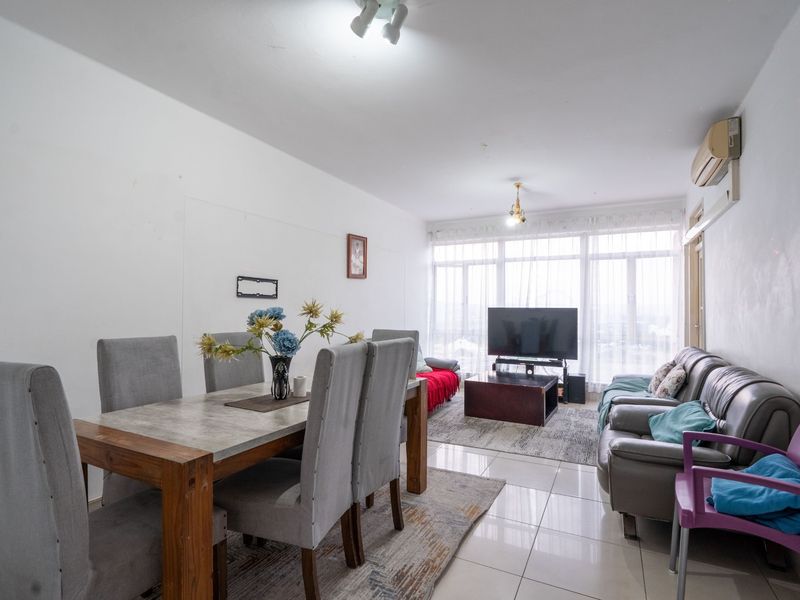 An open-plan living and dining area featuring tiled flooring, large windows providing natural light, and a wall-mounted air conditioning unit.