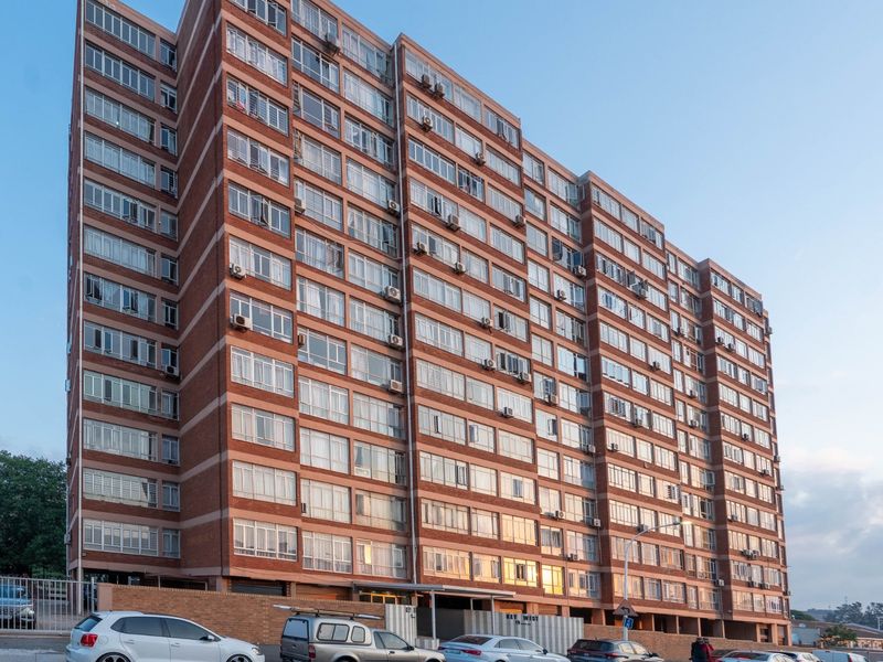 A multi-story residential apartment building featuring a classic red brick facade and extensive window glazing throughout the exterior elevation.