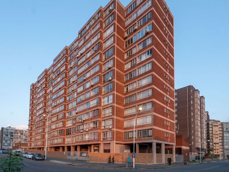A multi-story red brick apartment building featuring a prominent corner facade, ground-level parking access, and numerous window units.